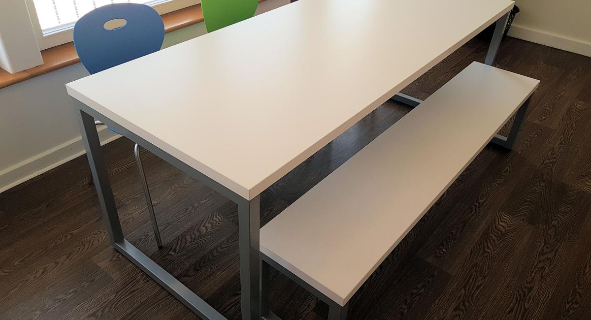 Steel frame bench table finished with a white top, partnered with coloured polypropylene chairs.