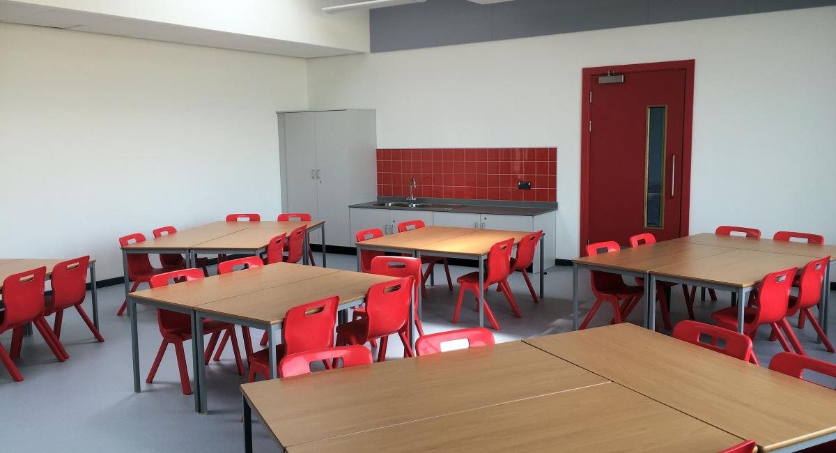Beech classroom tables partnered with red one-piece Postura+ classroom chairs.