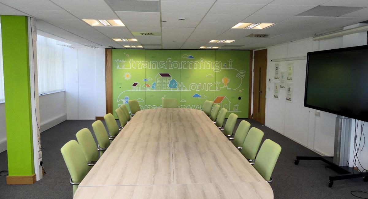 Meeting room table to seat 14 people or more finished in Nordic Ash with green upholstered meeting room chairs.